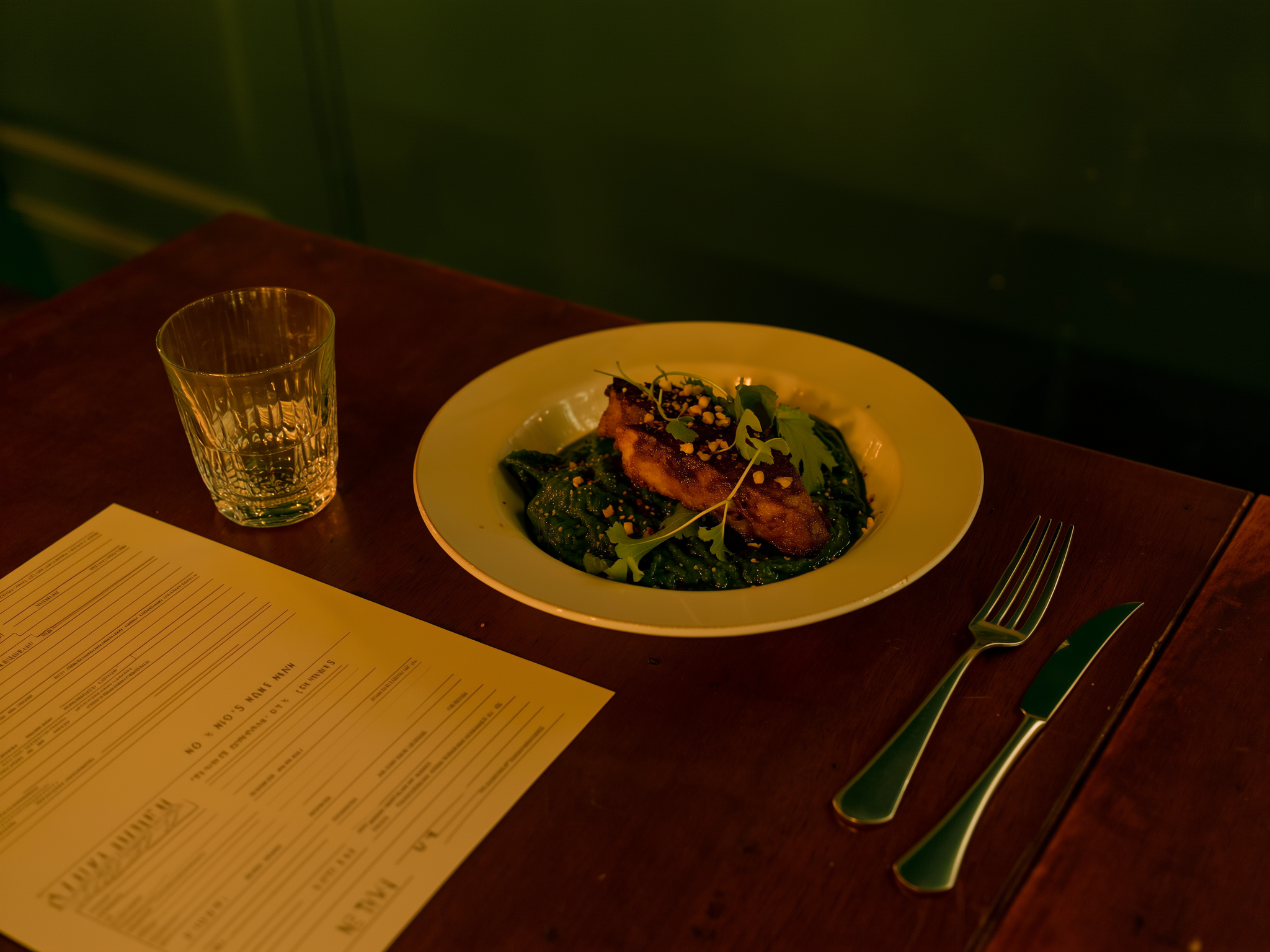 Krokant gebakken hoofdgerecht op groene kruidenpuree, opgediend aan een houten tafel